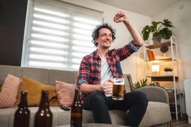 Yetişkin bir adam televizyonda maç izlerken ve evde bira içerken mutlu mesut tezahürat yapıyor.