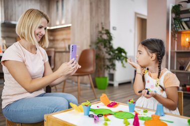 Bir anne kızının resmini çeker ve rahat oturma odalarında renkli mankenlerle resim yaparken eğlenir..