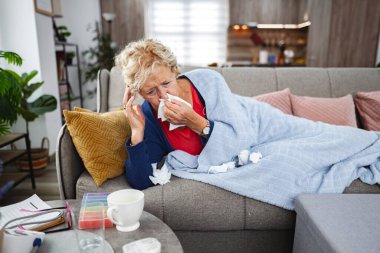 Yaşlı kadın kanepeye uzanır, kendini kötü hisseder ve etrafı mendillerle çevrilidir..