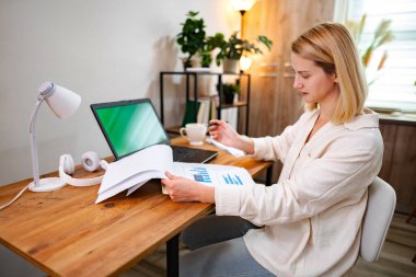 Kişi, sıcak çalışma alanındaki çizelgeleri ve raporları titizlikle gözden geçirir.