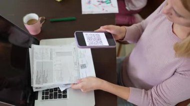 Ev organizasyonunda çalışan bir kişi, QR kodlarını akıllı bir telefonla tararken faturaları düzenler ve tüm belgelerin verimli bir şekilde hesaplandığından emin olur..