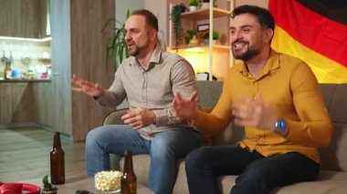 İki arkadaş evde spor müsabakalarını izlerken coşkuyla tezahürat yapıyor..