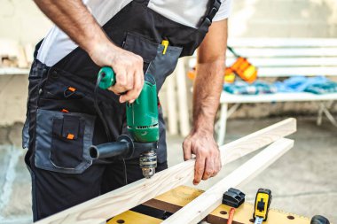 Tanımlanamayan erkek marangoz, açık havada tahta üzerinde elektrikli matkap kullanıyor..