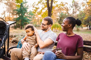 Karışık ırk çiftleri parktaki bir bankta oğullarıyla oturuyor..