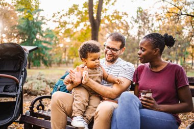 Karışık ırk çiftleri parktaki bir bankta oğullarıyla oturuyor..