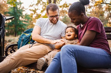 Karışık ırk çiftleri parktaki bir bankta oğullarıyla oturuyor..