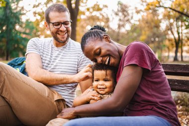 Karışık ırk çiftleri parktaki bir bankta oğullarıyla oturuyor..