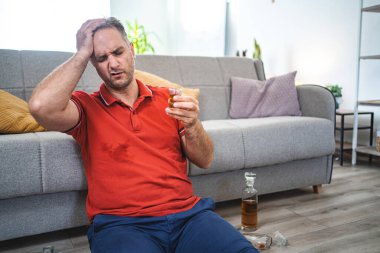 Olgun bir adam yerde oturup içki içiyor..