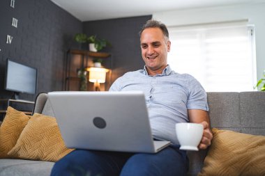 Koltukta dizüstü bilgisayar kullanan orta yaşlı beyaz bir adam..