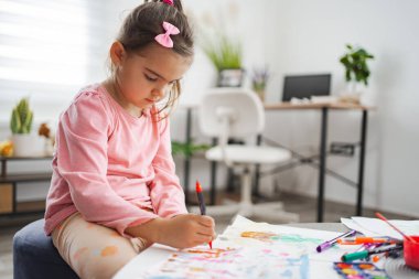 Bir çocuk masasında parlak işaretlerle çizim yapmaya derinden odaklanır..