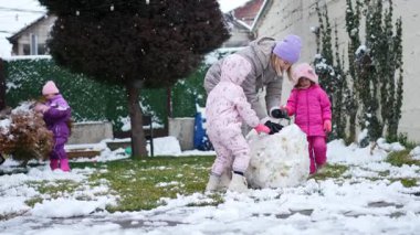 Çocuklar bahçende kar altında neşeyle bir kardan adam yapar..
