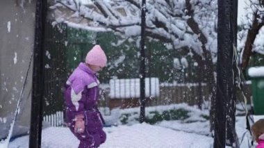 Mor kar giysili bir çocuk neşeyle trambolinde zıplıyor..