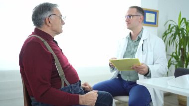 Bir doktor klinikte yaşlı bir hastayla sağlık sorunlarını tartışır..