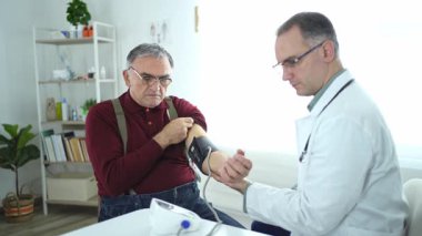 Bir doktor klinikteki yaşlı bir adamın kan basıncını dikkatle izler..