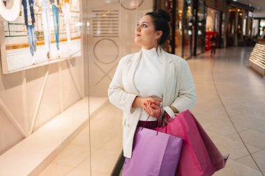 Renkli alışveriş torbaları taşıyan bir kadın vitrinlere bayılır..