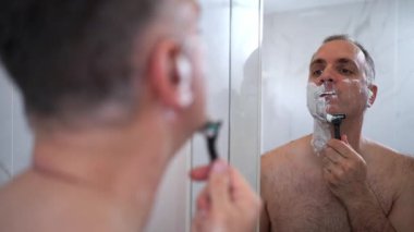 Bir adam güne yüzünü banyo aynasında dikkatlice tıraş ederek başlar. Yumuşak ışık, her vuruşta temiz bir görünüm elde etmeye odaklanırken sabah titreşimini arttırır..