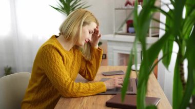 Sıcak ve cezbedici bir çalışma alanında, örgü kazaklı bir kadın, yeşil ve yumuşak ışıklandırmayla çevrili laptopunda zor bir görevle uğraşırken stres ve hayal kırıklığını ifade eder..