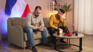 İki arkadaş düşünceli bir sessizlik içinde, rahat bir dekor ve içeceklerle çevrili olarak otururlar..