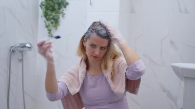 Modern bir banyoda oturan bir kadın saçını boyar..