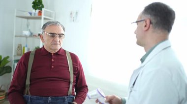 Bir sağlık uzmanı klinikte yaşlı bir adamla sağlığı tartışıyor.