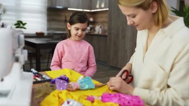 Bir anne, kızı zevkle izlerken renkli kıyafetler hazırlar..