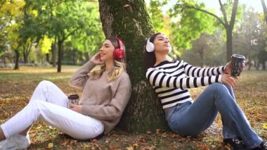 İki arkadaş, canlı bir parkta kahveyi yudumlarken sonbahar havasının tadını çıkarıyor..