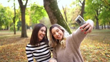 Renkli bir parkta güneşli bir günün tadını çıkarırken iki arkadaş gülümsüyor.