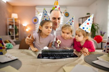 Çocuklar bir pasta etrafında toplanır, dilek tutup mumları üflemeye hazırdırlar..