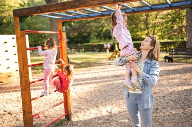 Gülümseyen anne, sevimli kızının oyun parkına çıkmasına yardım ediyor..