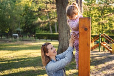 Gülümseyen anne, sevimli kızının oyun parkına çıkmasına yardım ediyor..