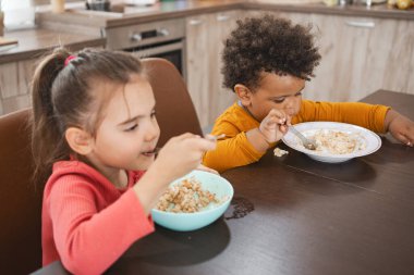 İki küçük çocuk kahvaltılarını bir mutfak masasında mutlu bir şekilde yiyorlar..