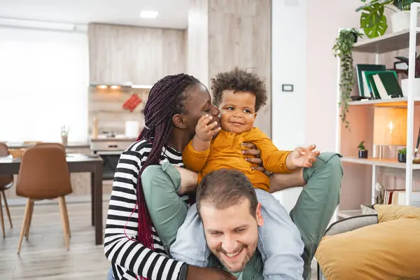 Bir anne ve baba, küçük evladıyla evde şakalaşarak etkileşim halindedir..