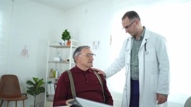 Doktor, iyi aydınlatılmış bir klinikte yaşlı bir hastaya destek sunar.