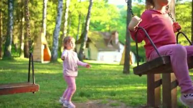 Genç bir kız, canlı ağaçlar ve sıcak güneş ışığıyla çevrili güzel bir parkta neşeyle sallanıyor. Çocukluk sevincinin tasasız anlarını kucaklarken gülüşü havayı dolduruyor..