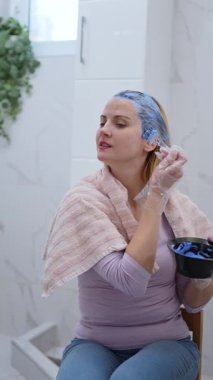 Bir insan rahat bir şekilde otururken saçına koyu mavi renk sürer..