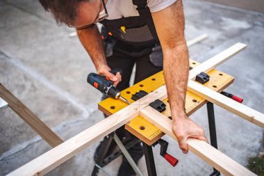 Olgun erkek marangoz, tahtadan bir tahta üzerinde elektrikli tornavida kullanıyor..