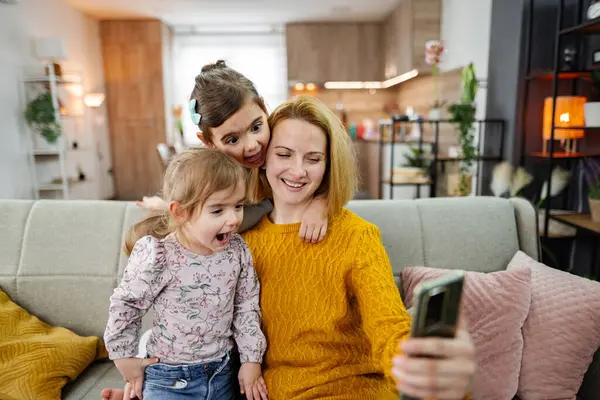 Anne ve üç kızı kanepede oturup evdeki oturma odasında selfie çekiyorlar..