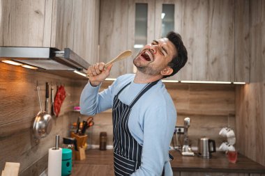 Kahverengi saçlı adam mutfaktaki ahşap sobanın içinde neşeyle şarkı söylüyor..