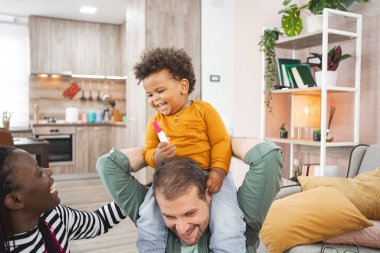 Neşeli bir çocuk evde babasının omuzlarında otururken gülümsüyor..