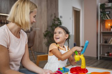 Genç bir kız, annesinin yanında renkli oyuncaklarla oynarken ışıl ışıl gülümsüyor..