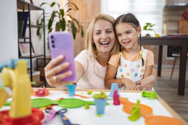 Bir anne ve kız, evde renkli plastiklerin arasında eğlenceli bir selfie çekerken gülümsüyor..