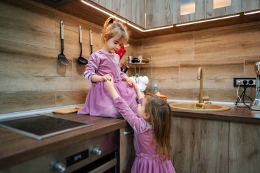 İki genç kız kardeş, mutfak eşyaları ile çevrili neşeli bir anı paylaşırken sıcak, modern bir mutfakta neşeli ifadeler sergilerler..