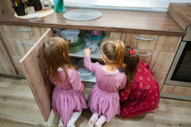 Doğal ışıkla dolu sıcak bir mutfakta, üç güzel elbiseli genç kız bir dolaptan canlı tabaklar hazırlıyorlar..