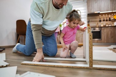 Bir baba ve küçük kızı sıcak, davetkar oturma odalarında mobilya montajı yapmak için birlikte çalışıyorlar. Araçlar ve parçalar özel bir bağ anlarını paylaştıkça etraflarını sarar..