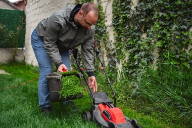 Bahçıvan canlı çimlerini korumaya odaklanıyor. Çim biçme makinesinden yeni kesilmiş çim kesitlerini kovaya boşaltıyor. Çevre bereketli, huzurlu bir akşam atmosferini vurguluyor..