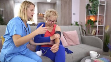 Empati kurabilen bir sağlık uzmanı, evdeki son sınıf öğrencisine sıcak bir oturma odası ortamında sağlık ve refahı kontrol ediyor. Etkileşimde rahatlık ve destek vurgulanıyor.