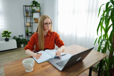 Genç bir kadın dikkatlice masasında çalışıyor, etrafı bitkiler ve ışıklarla çevrili..