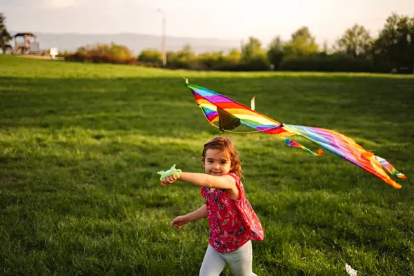 Neşeli genç bir kız çimenli arazide koşuyor, elinde hafif bir esintide dans eden canlı bir uçurtma tutuyor. Sıcak güneş ışığı sahneyi yıkıyor, neşeli bir oyun atmosferi yaratıyor..