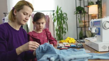 Bir anne kızına renkli malzemelerle çevriliyken dikiş dikmeyi öğretir..