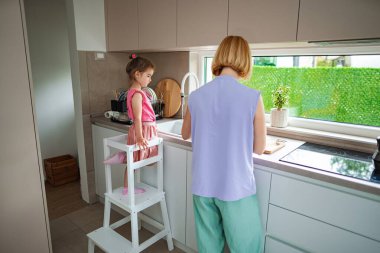 Annesi yemek hazırlarken genç bir kız yakından izler..